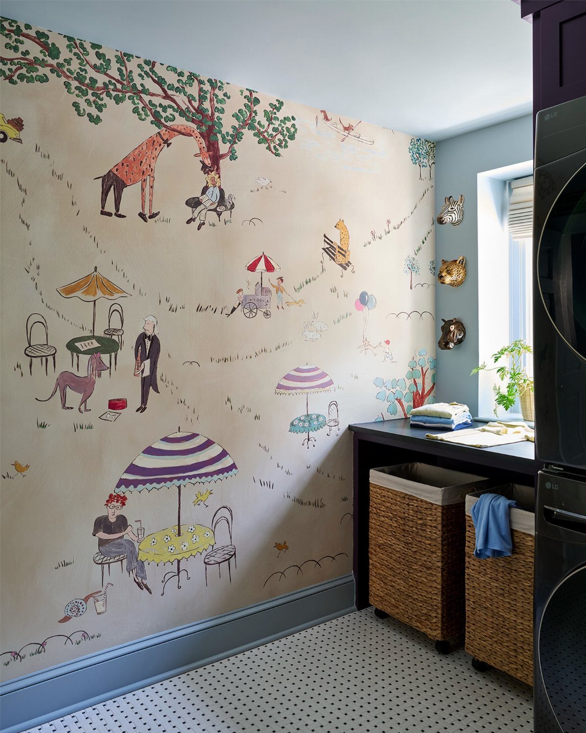 Whimsical illustrated wallpaper in a laundry room with wicker baskets and dark countertops.