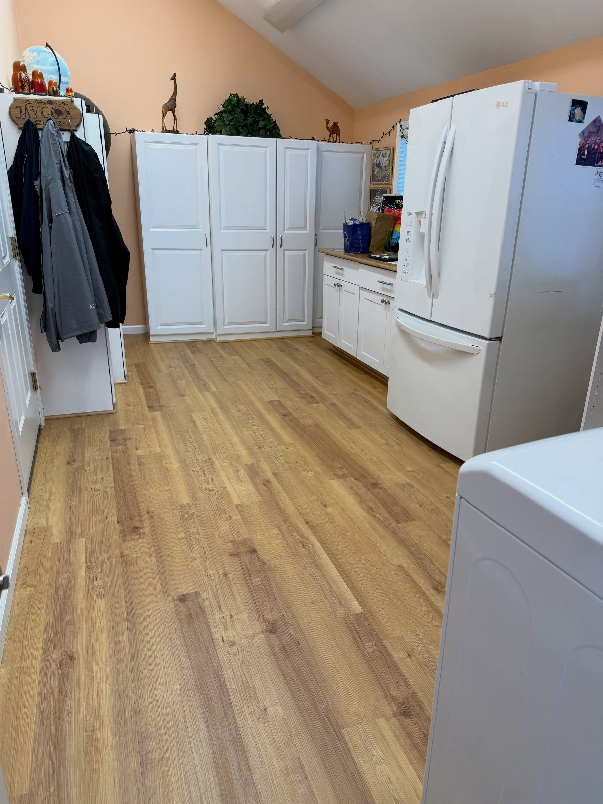 Wood-look vinyl flooring in a basement laundry room with white cabinets and appliances.