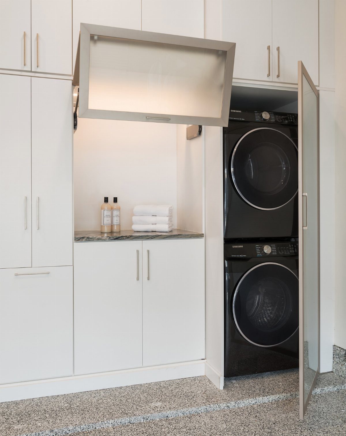 Stacked black washer and dryer in white garage cabinetry with epoxy flooring