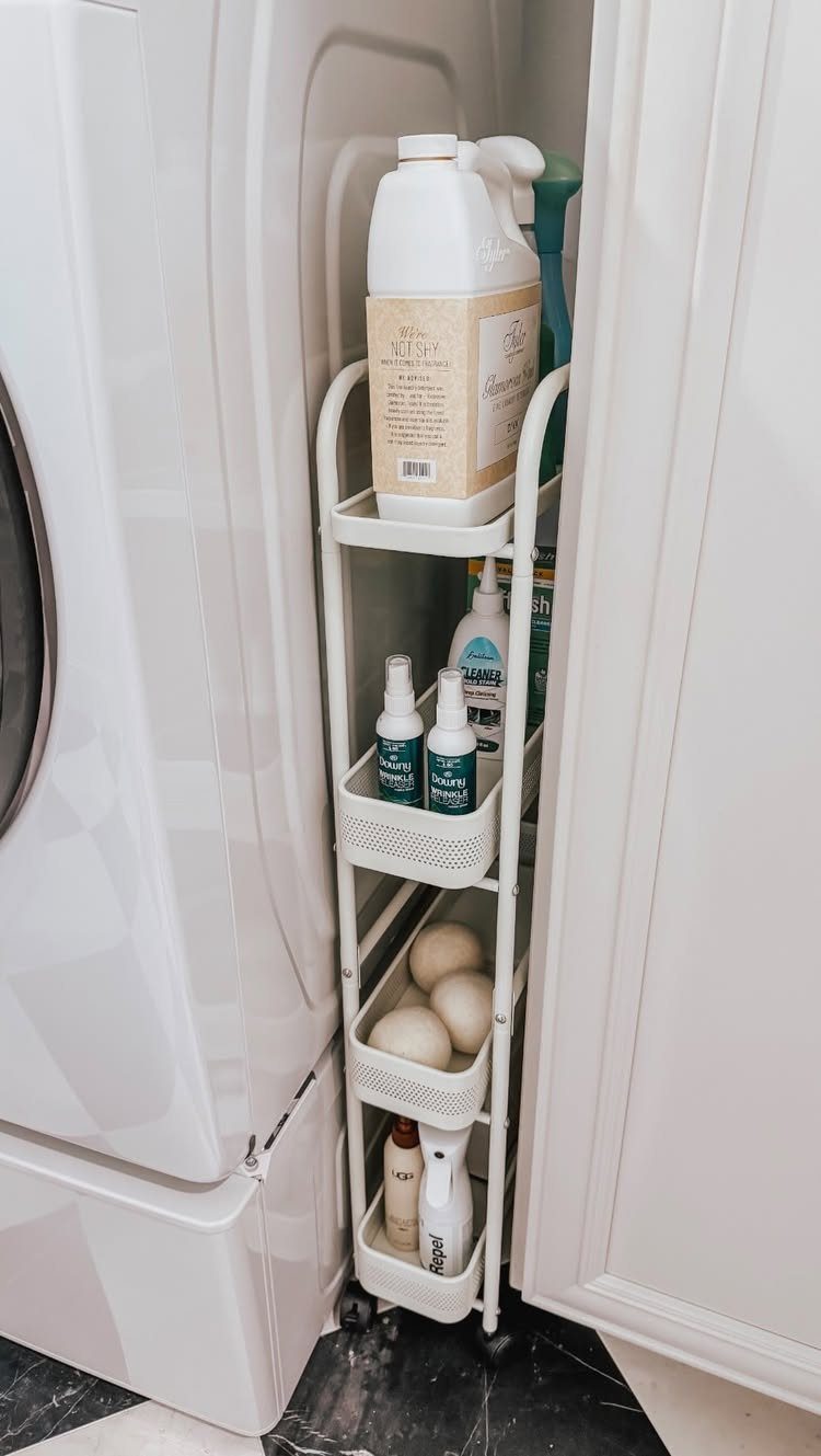 White rolling storage cart with laundry supplies between a washer and cabinet.