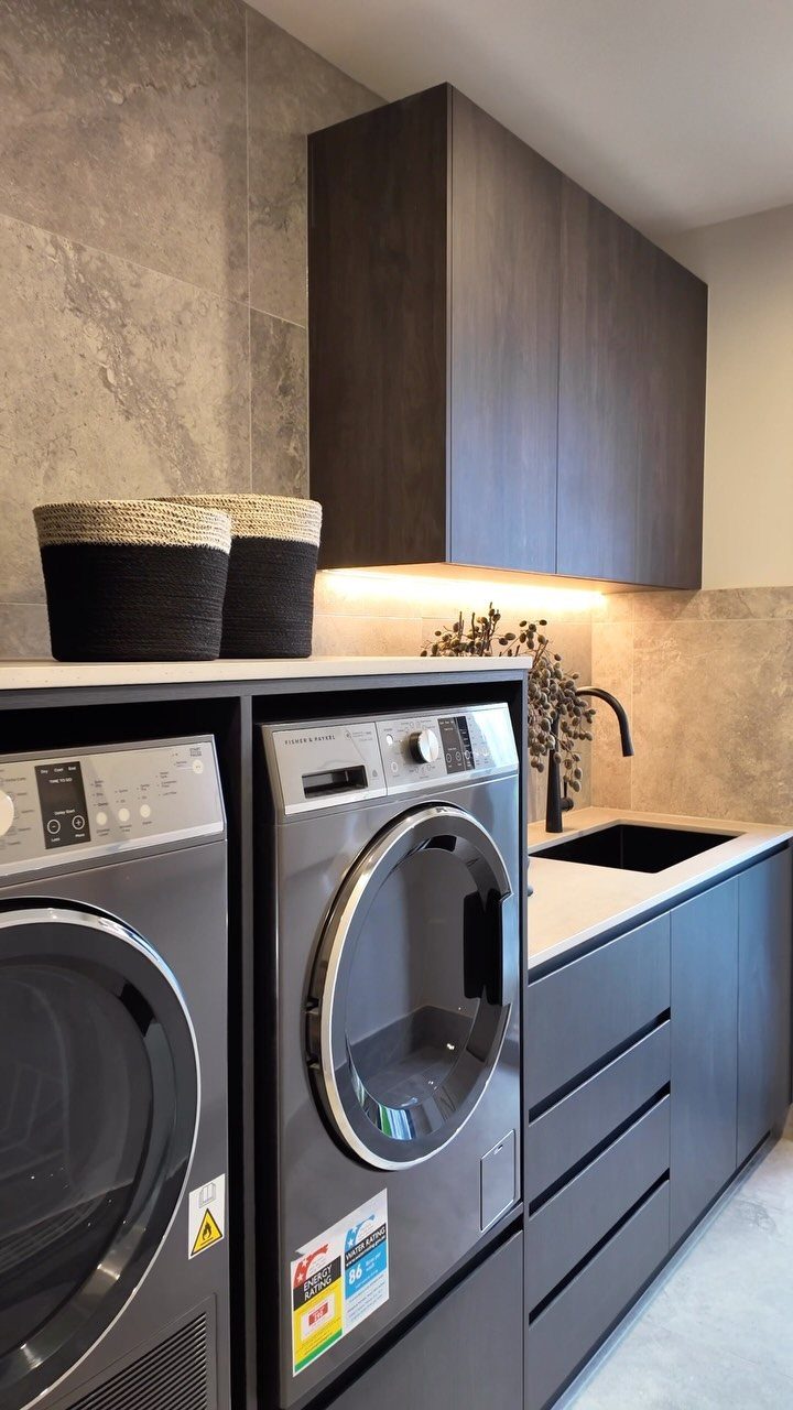 Dark grey uniform cabinetry and washing machines in a modern laundry room setup.