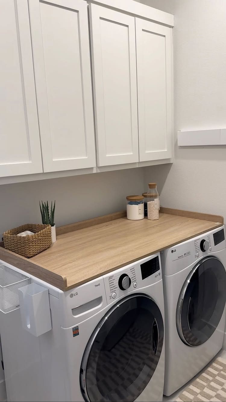 Light wood countertop over white washing machines with white cabinets above