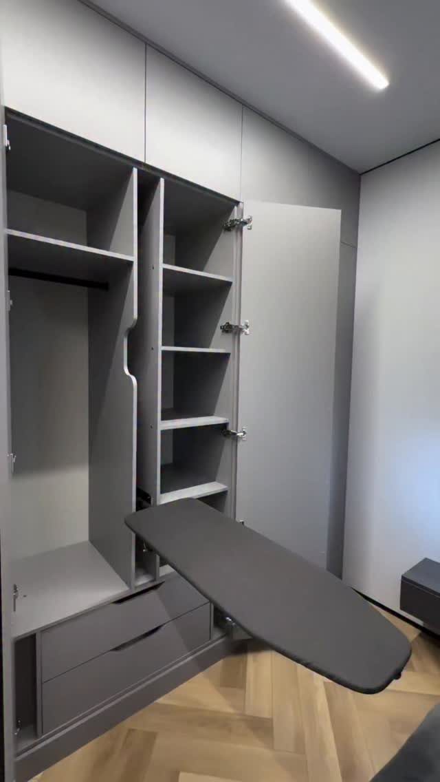 Grey built-in storage unit with shelves and a pull-out ironing board in laundry room.