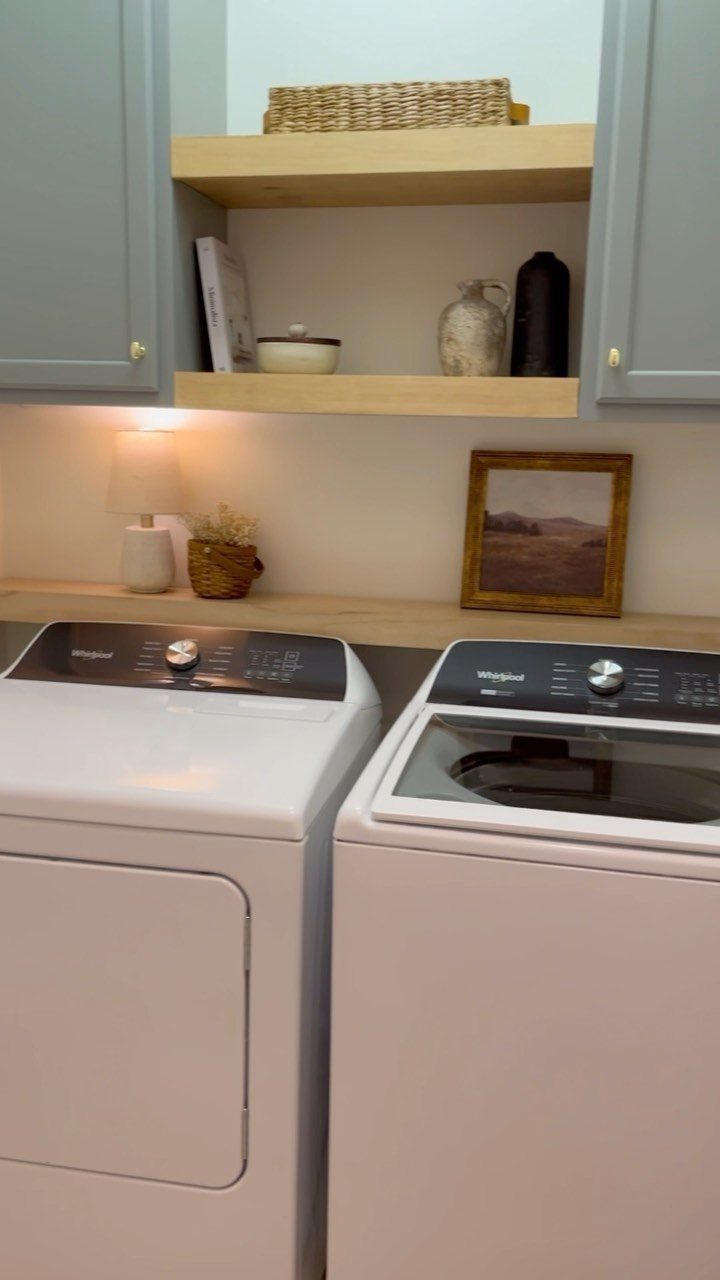 White washer and dryer with a light wood countertop and blue cabinetry above.