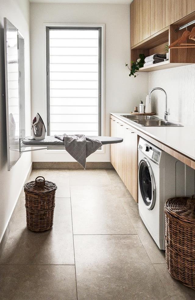 Wall-mounted ironing board extended in a modern laundry room with wood cabinets.
