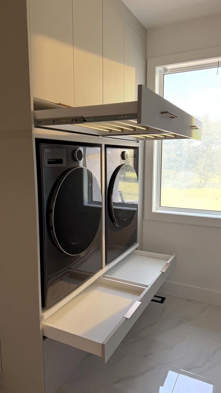 White pull-out drying rack extended above dark grey laundry machines in white cabinetry.
