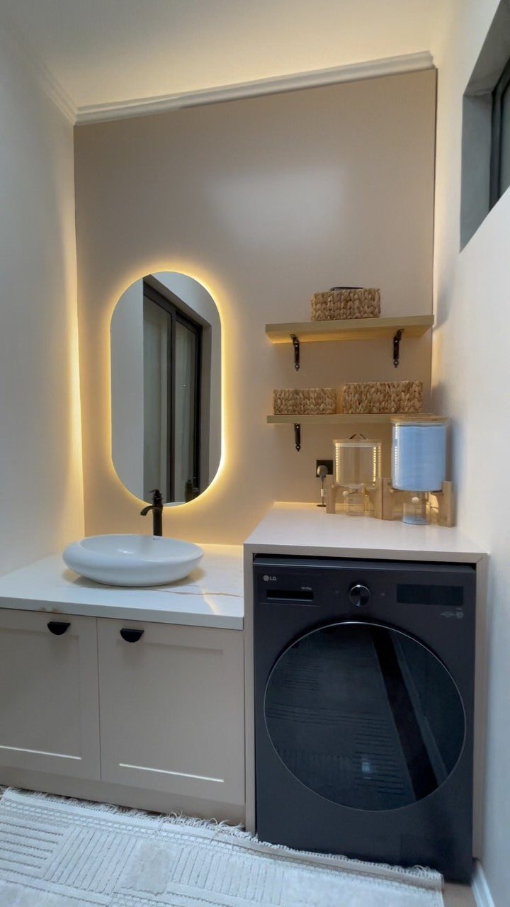 Modern laundry room with a dark washing machine, vessel sink, and backlit mirror.