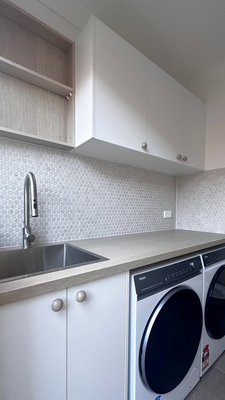 Modern laundry room with white cabinetry, grey countertops, and side-by-side washer and dryer.