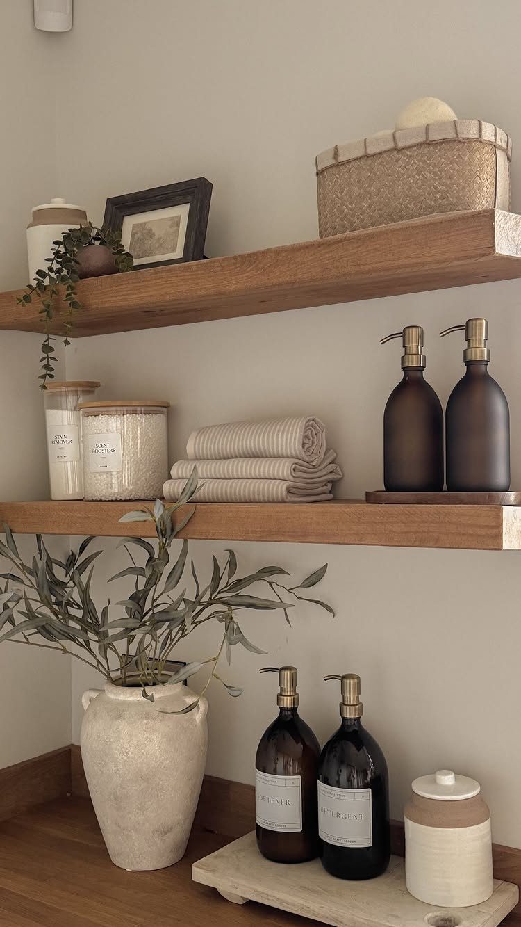 Wooden floating shelves with neutral decor, towels, and soap dispensers in a room.