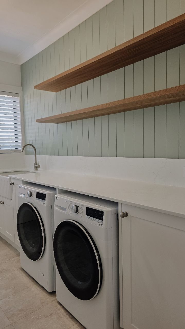 White cabinetry and countertops in a laundry room with floating wooden shelves.