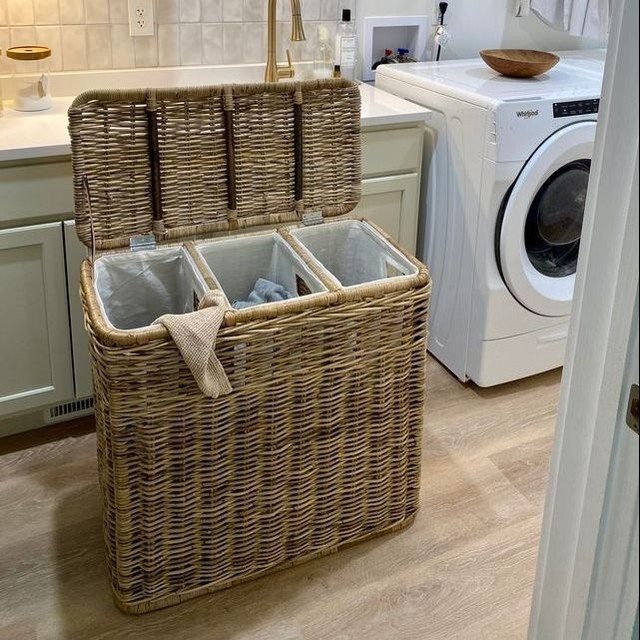 Three-compartment wicker laundry hamper with white liners in a bright laundry room