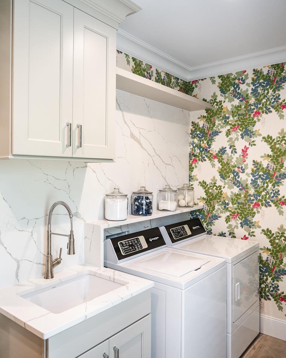 Laundry room with white appliances and bold floral wallpaper on the side wall.
