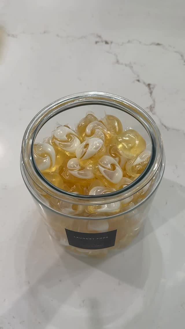 Clear glass jar filled with laundry detergent pods on a white marble countertop