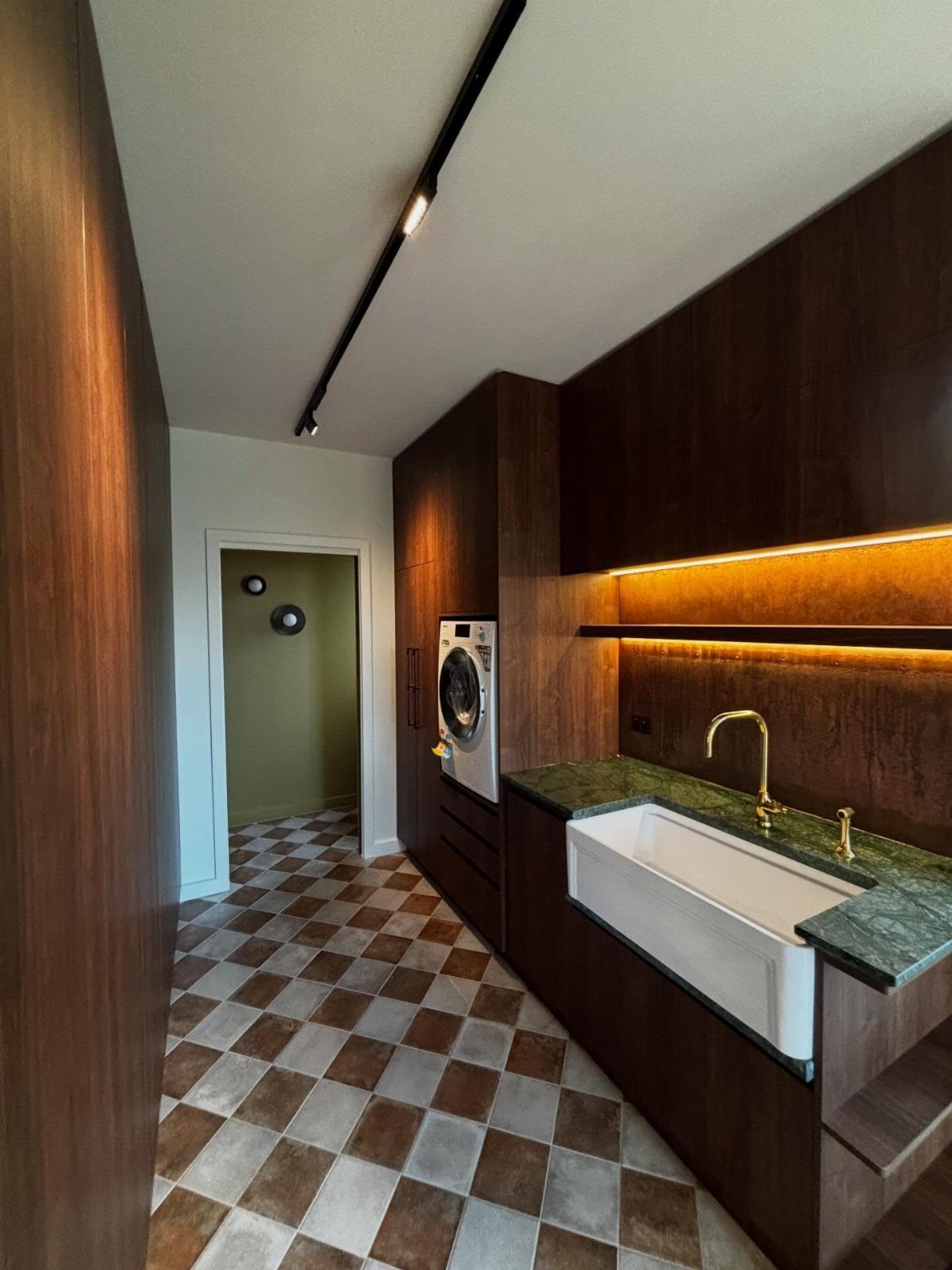 Narrow laundry room with dark wood cabinets, white sink, and checkered tiled floor.