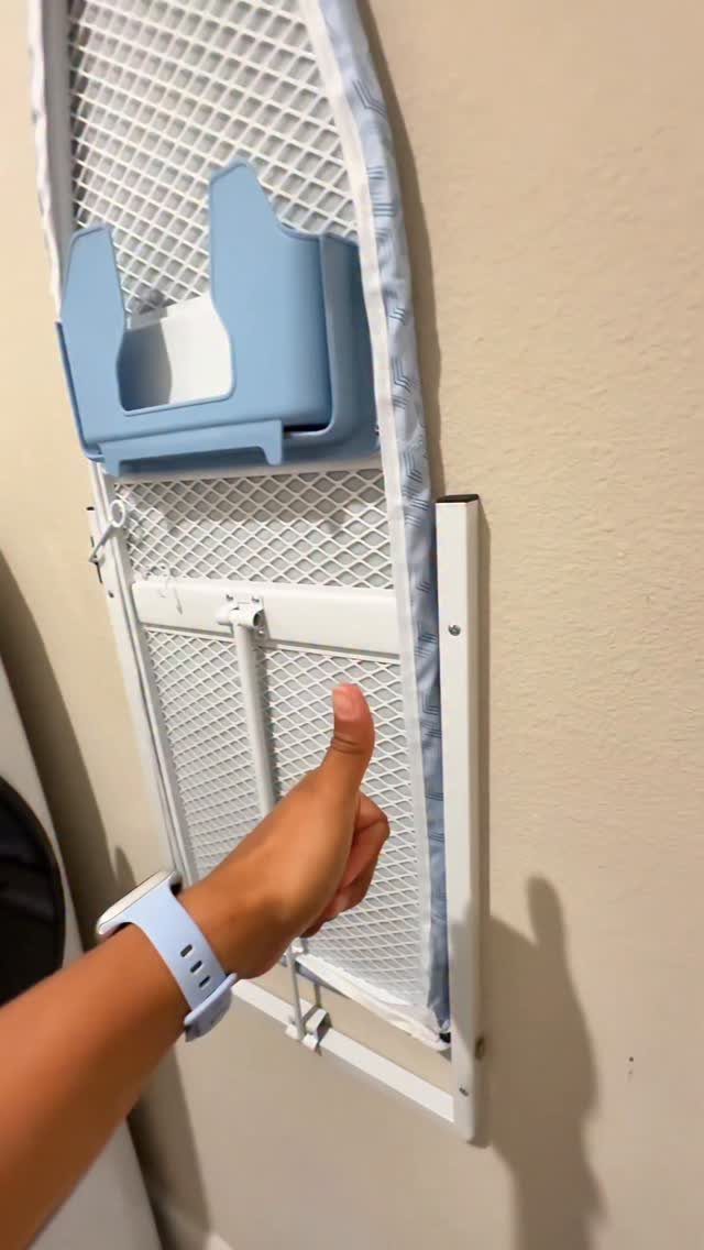 Wall-mounted fold down ironing board with a blue accessory on a beige wall.