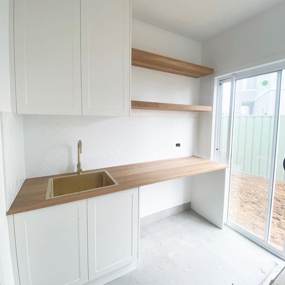 White utility room with light wood floating shelves and a matching wooden countertop.