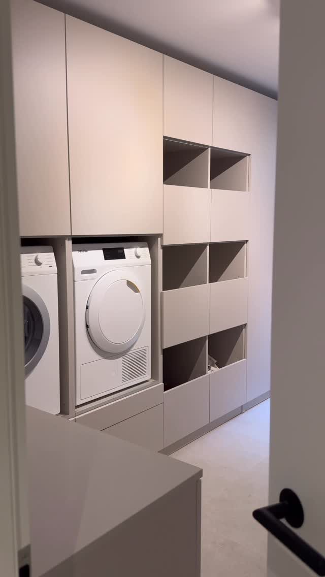 White built-in tall cabinets and open shelving surrounding a laundry washer and dryer.