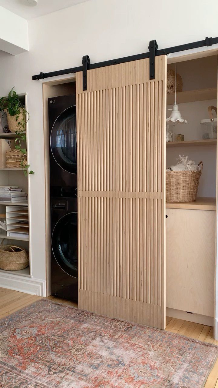 Light wood slatted barn door sliding over stacked black washer and dryer units.