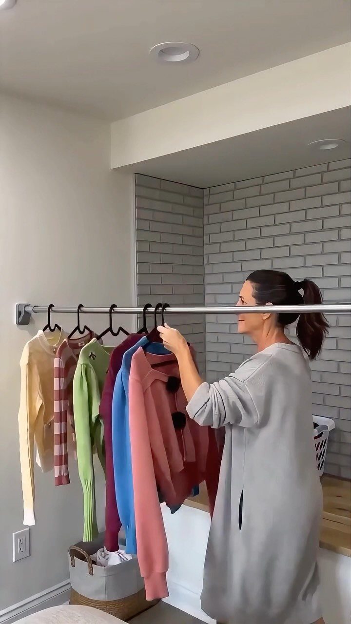 Woman hanging colorful clothes on a silver tension rod in a laundry room.