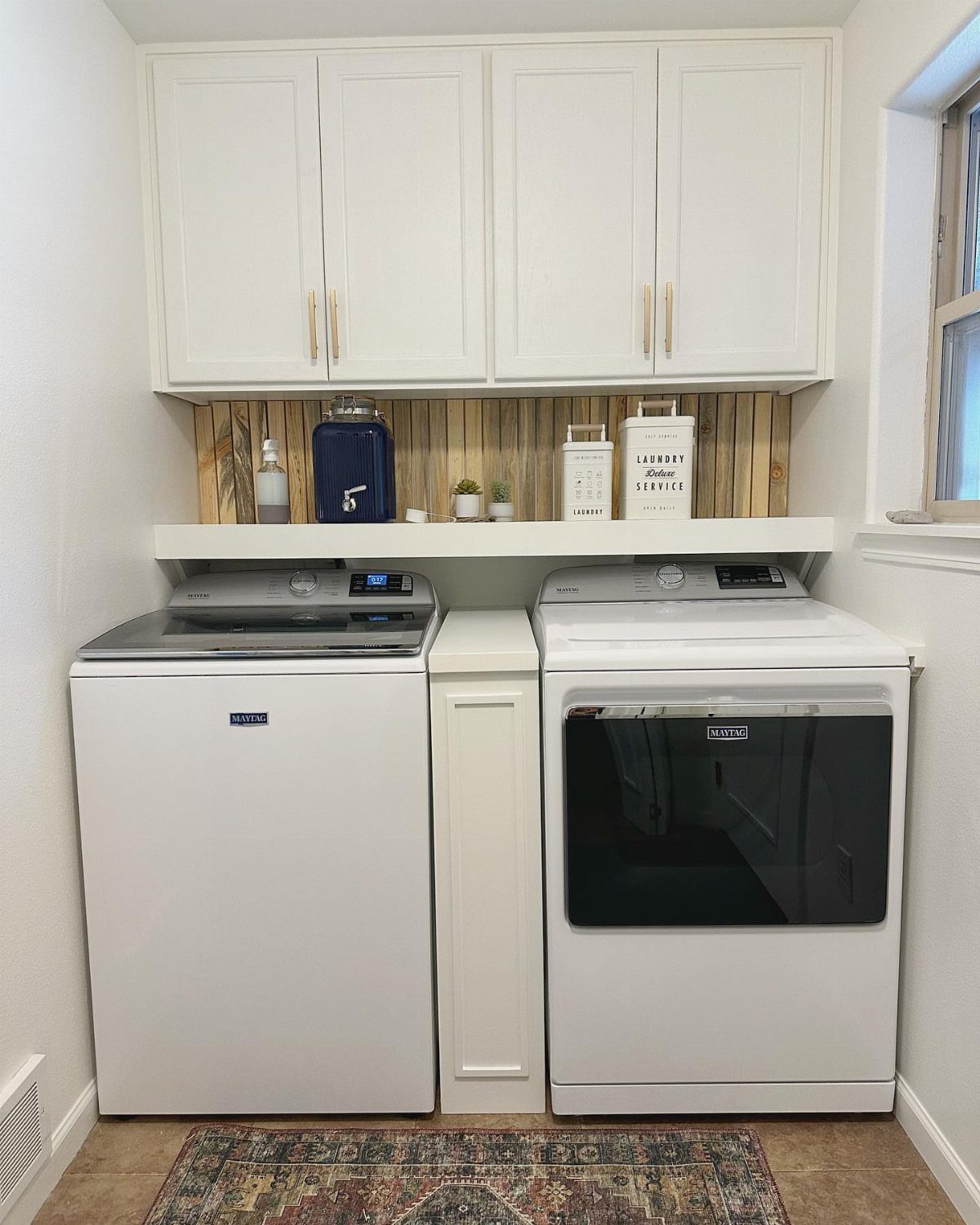 White top-loading washing machine and dryer under white cabinets in a laundry room