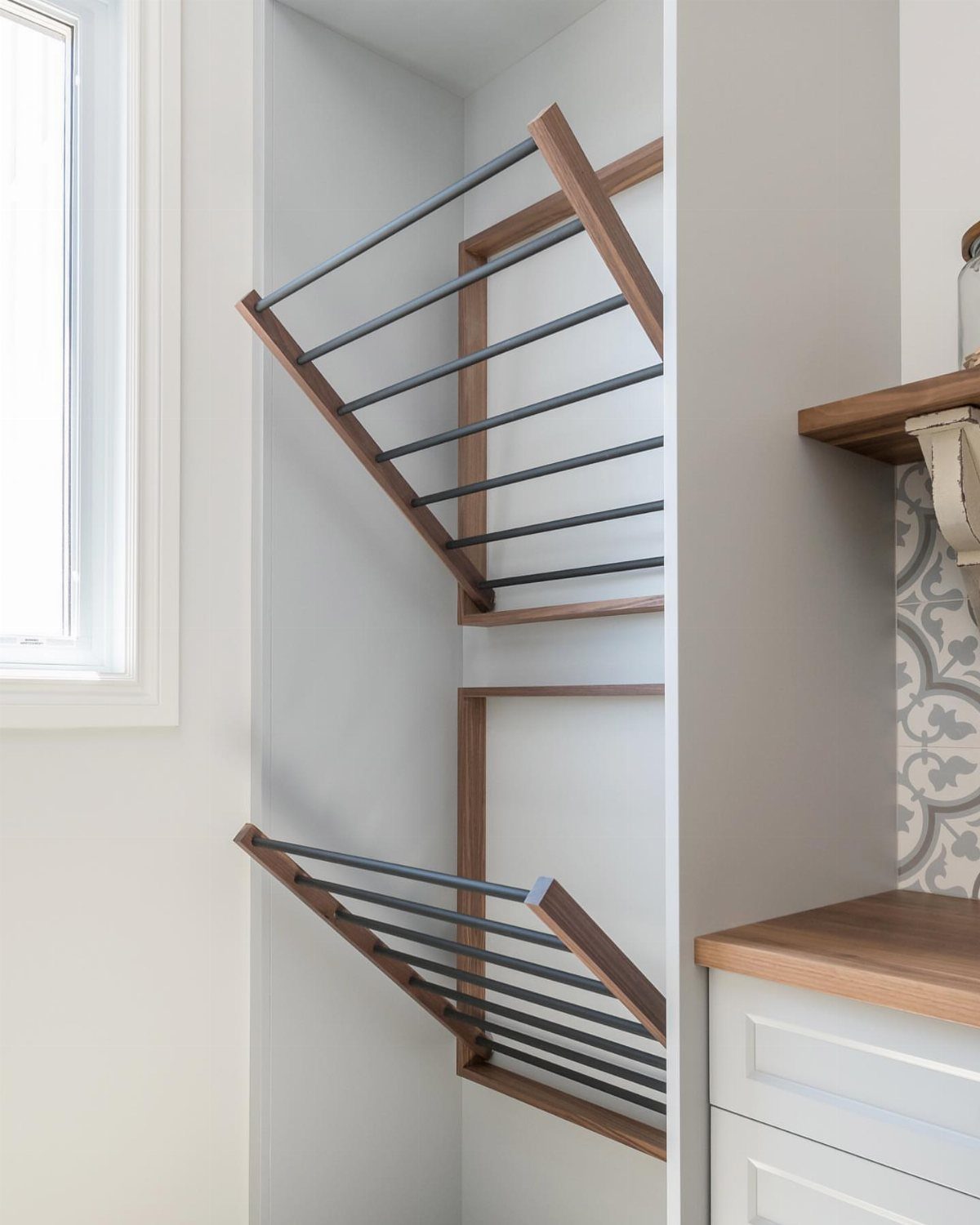 Wall-mounted drying racks with black bars and wooden frames in a white nook.