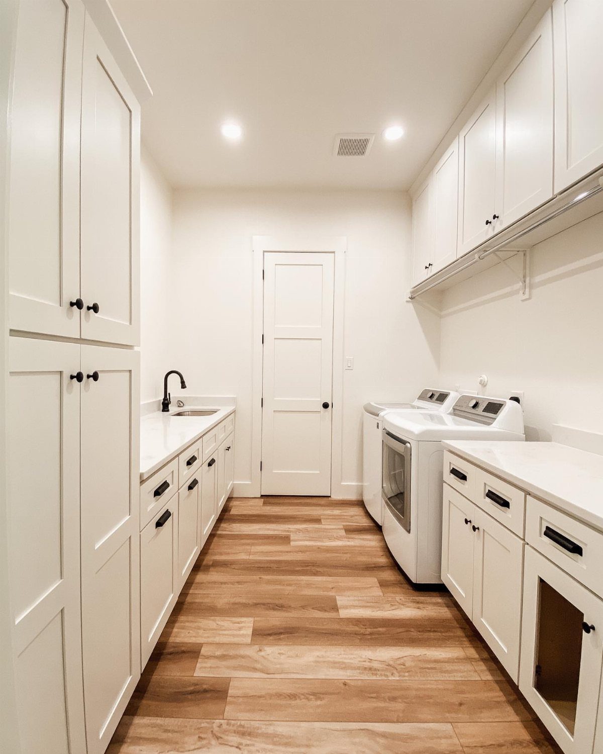 Laundry room with white cabinets and recessed ceiling lights over wood floors