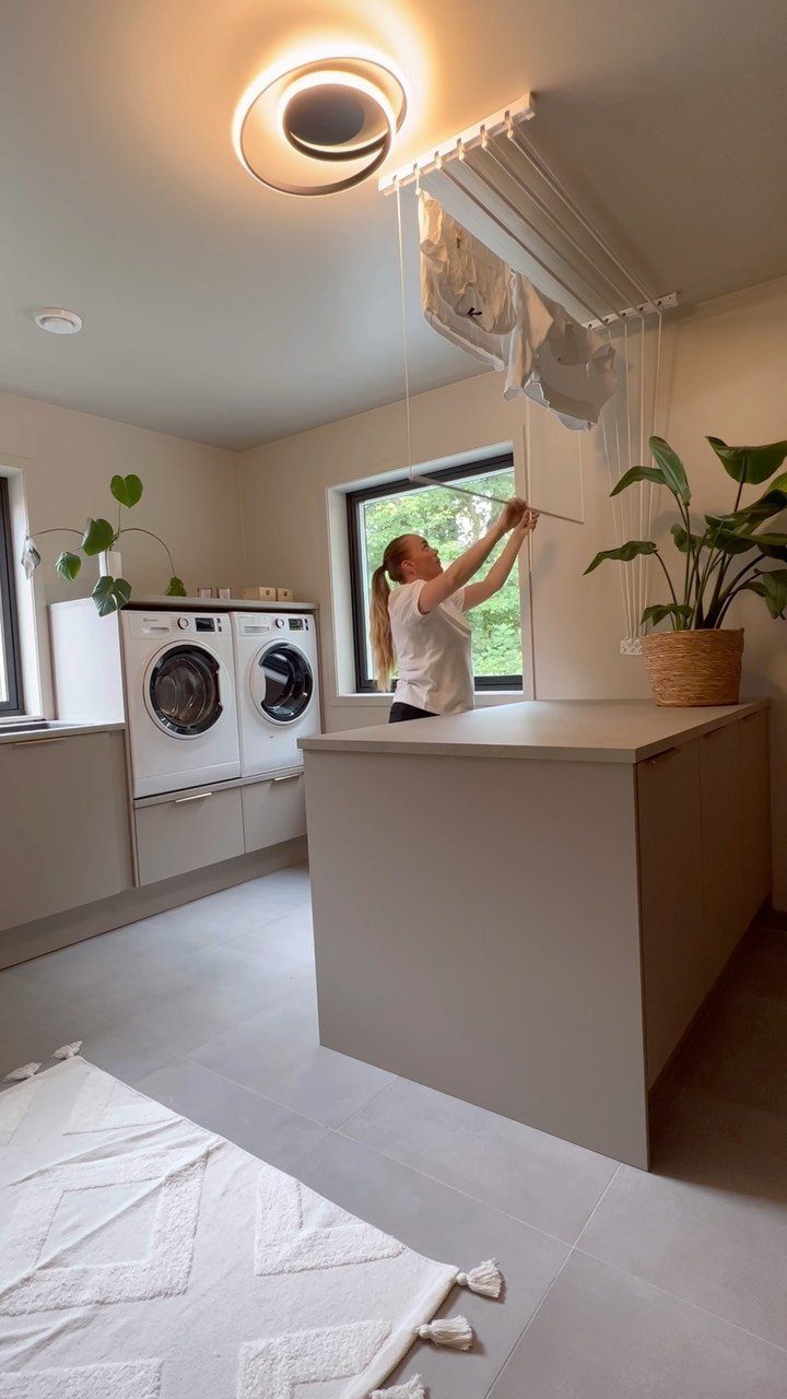 Woman lowering a white ceiling drying rack in a modern laundry room