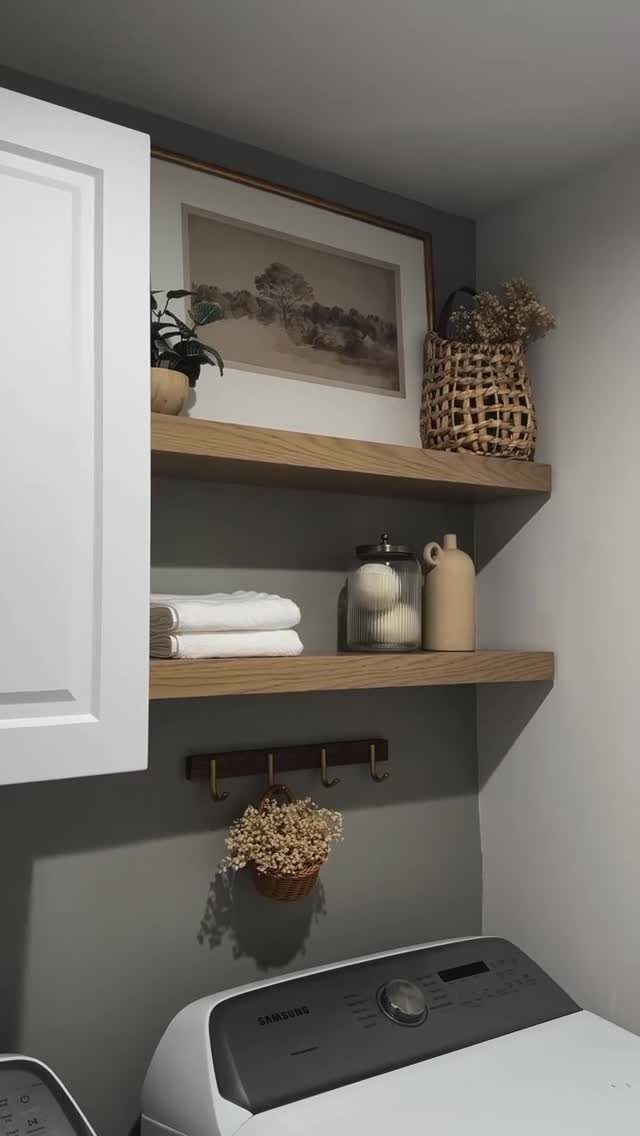 Two light-wood floating shelves with storage bins and towels above a washing machine.