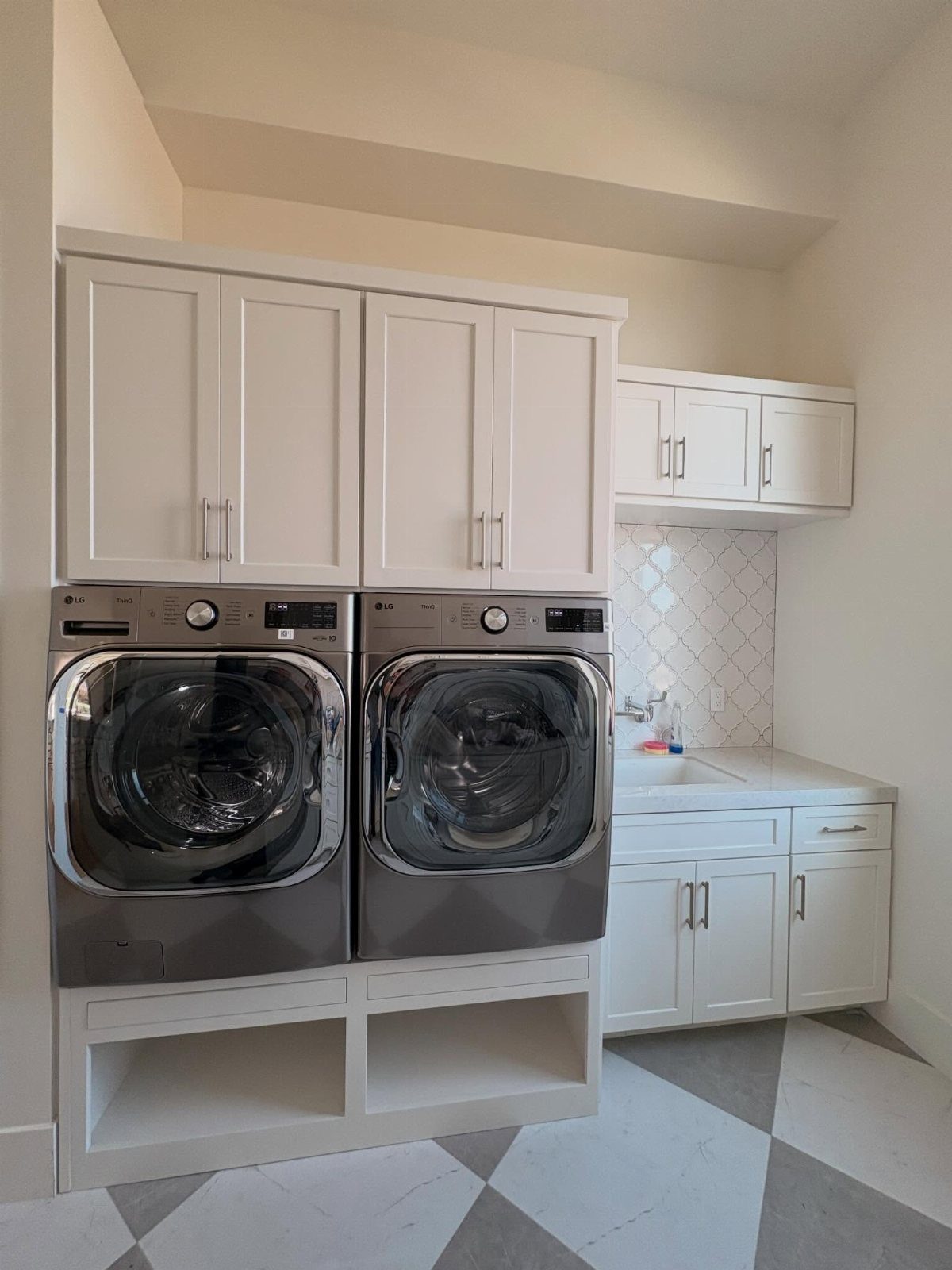 White built-in cabinets surrounding two metallic grey laundry machines in a modern room.