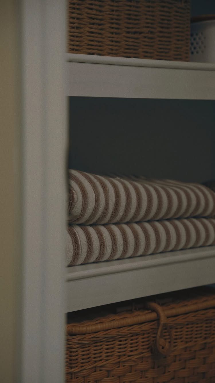 White wooden shelves holding folded striped towels and woven wicker storage baskets.