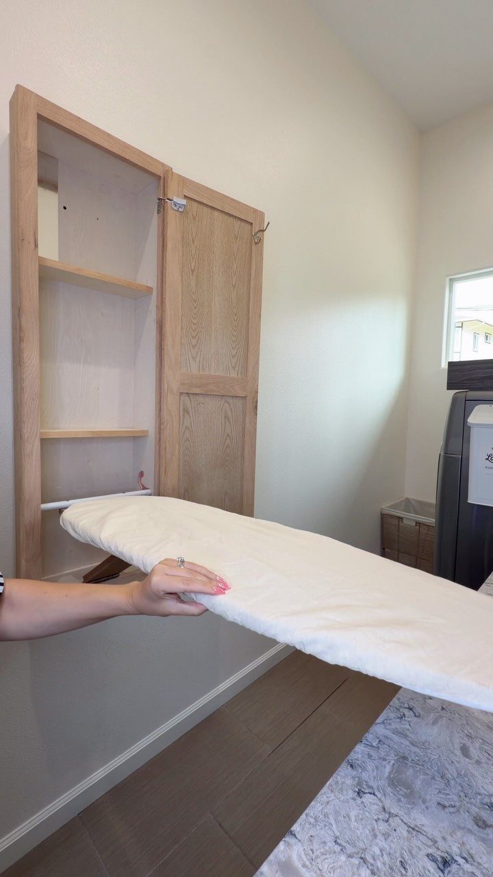 White ironing board folded down from a light wood wall-mounted storage cabinet.