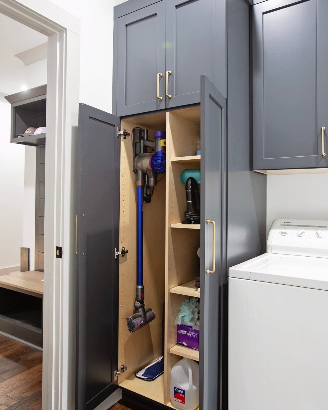 Grey laundry cabinet with interior shelving holding a vacuum and cleaning supplies.