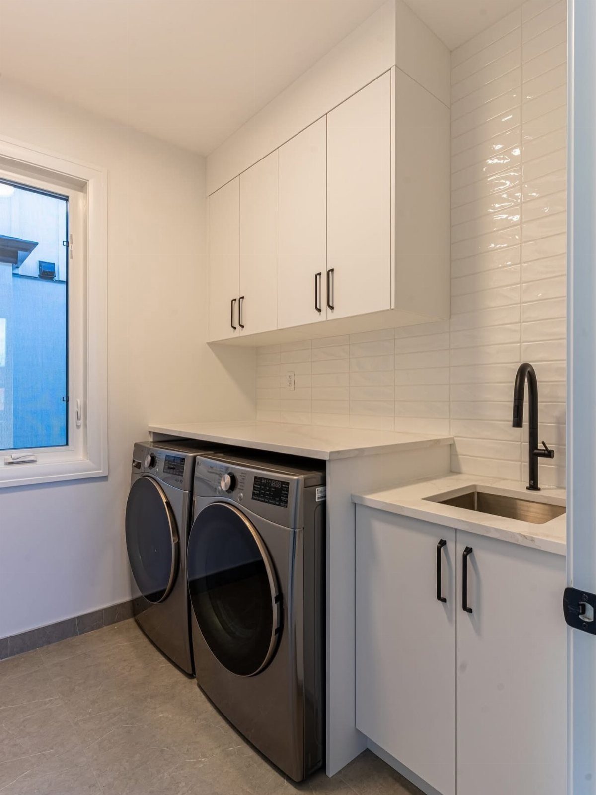 White laundry room with grey appliances, white cabinetry, and a small utility sink.
