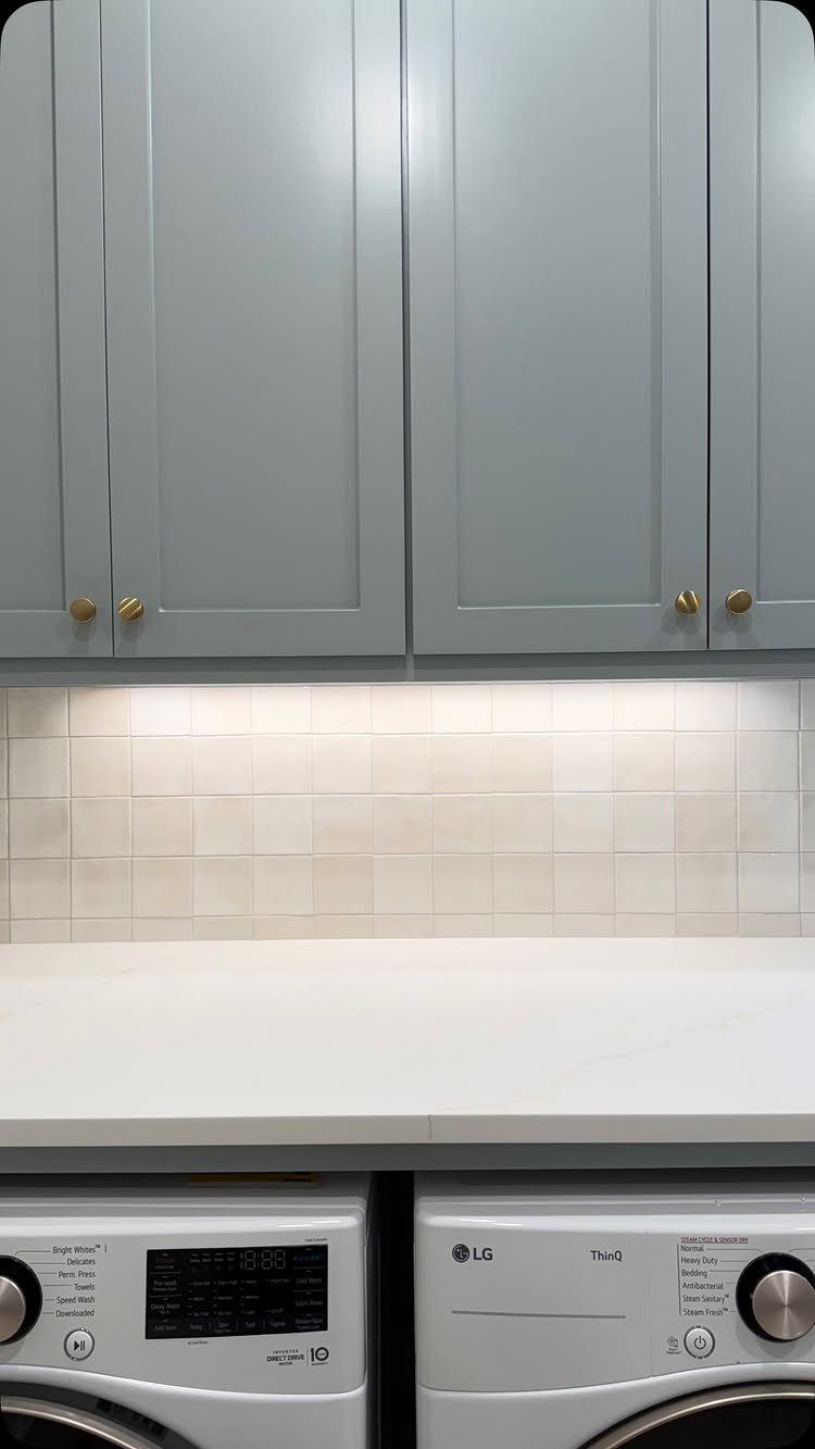 Blue-gray laundry room cabinets above white countertops and front-loading washing machines.