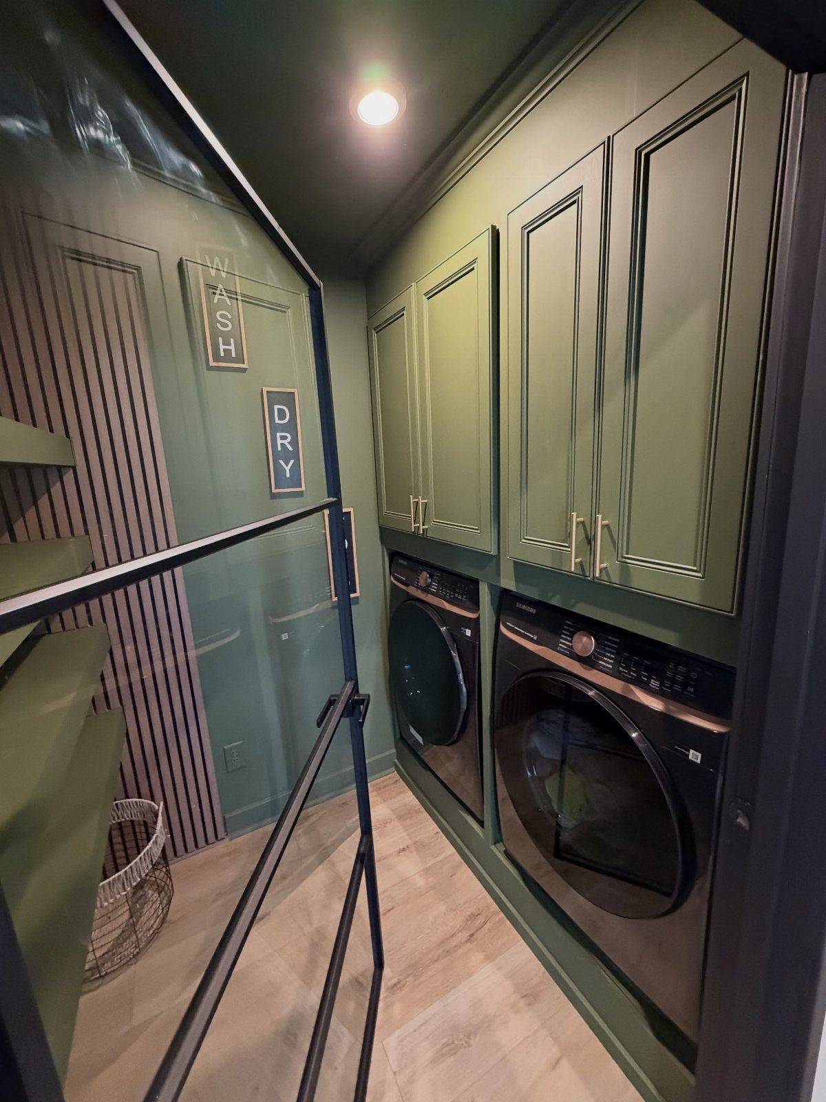 Olive green laundry room with matching cabinets and dark front-loading washing machines.