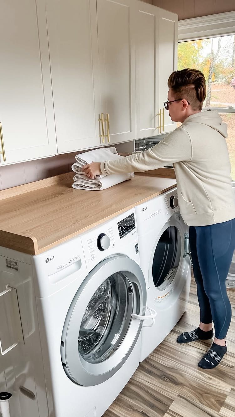 Person folding white towels on a wooden counter above white laundry machines.