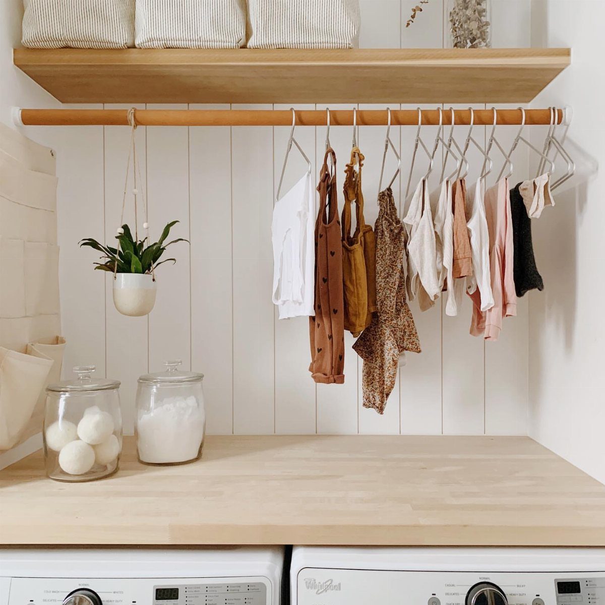 Wooden hanging rod below a shelf with children's clothes on white hangers.