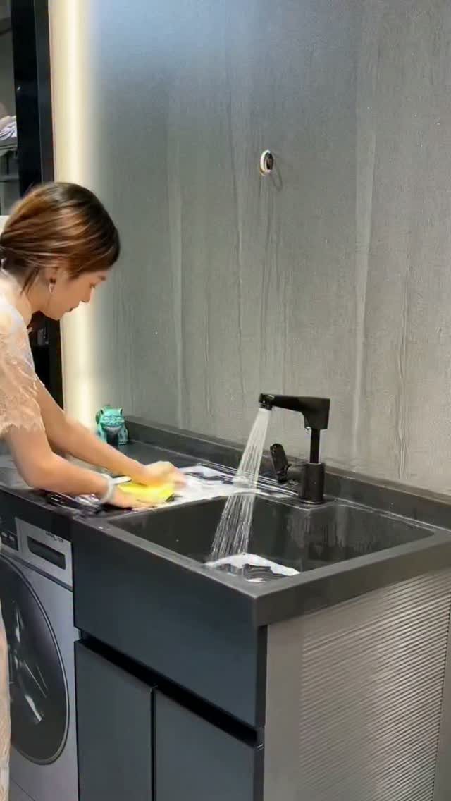 Woman scrubbing an item in a dark grey cabinet-mounted utility sink in a laundry room.