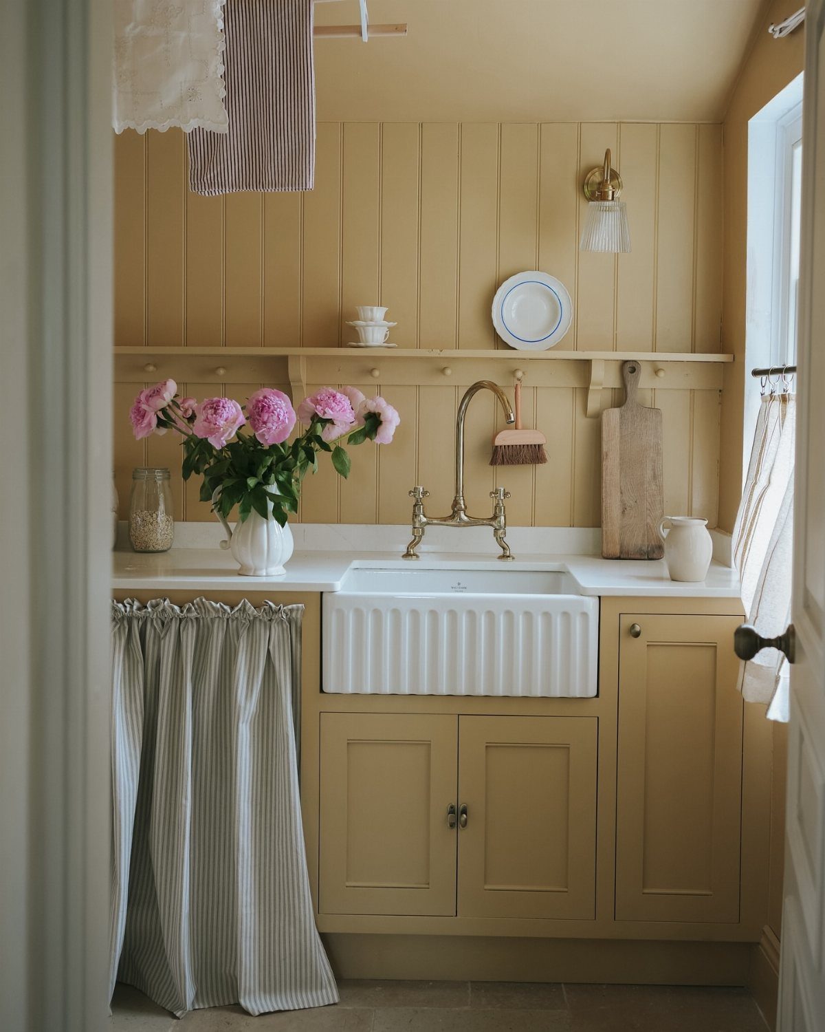 Farmhouse apron sink in a tan wooden cabinet with pink peonies and brass faucet.