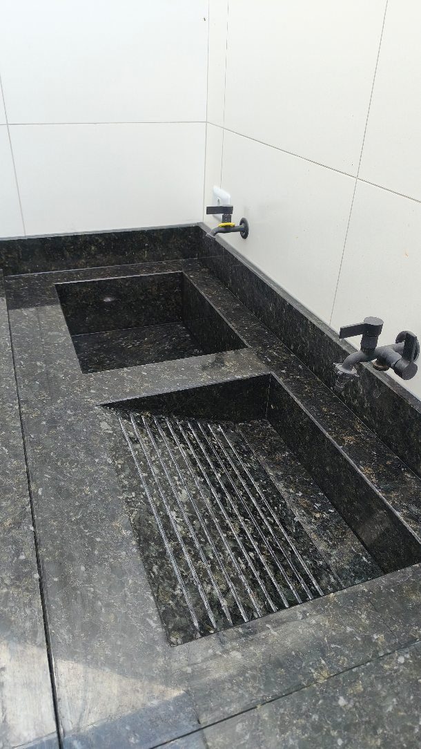 Dark grey granite utility sink with two basins and black faucets against white tiles.