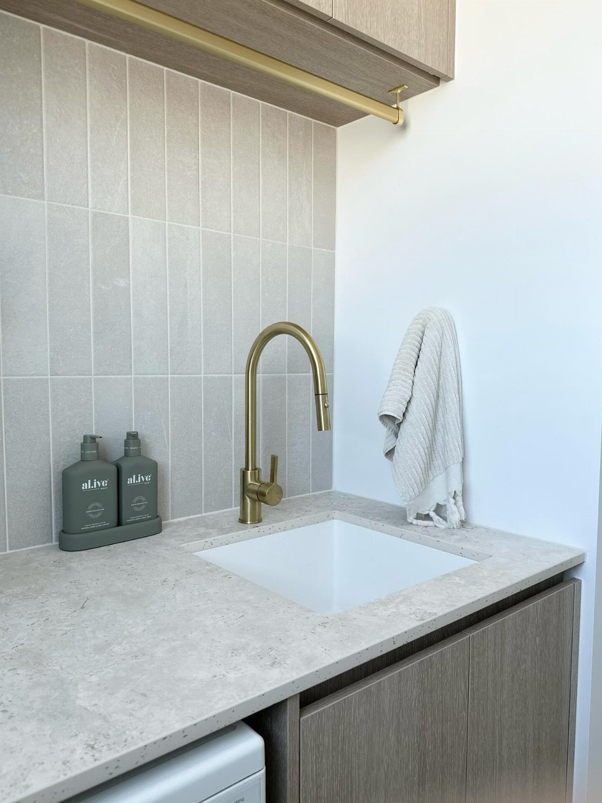 White utility sink with gold faucet and light grey vertical wall tiles.