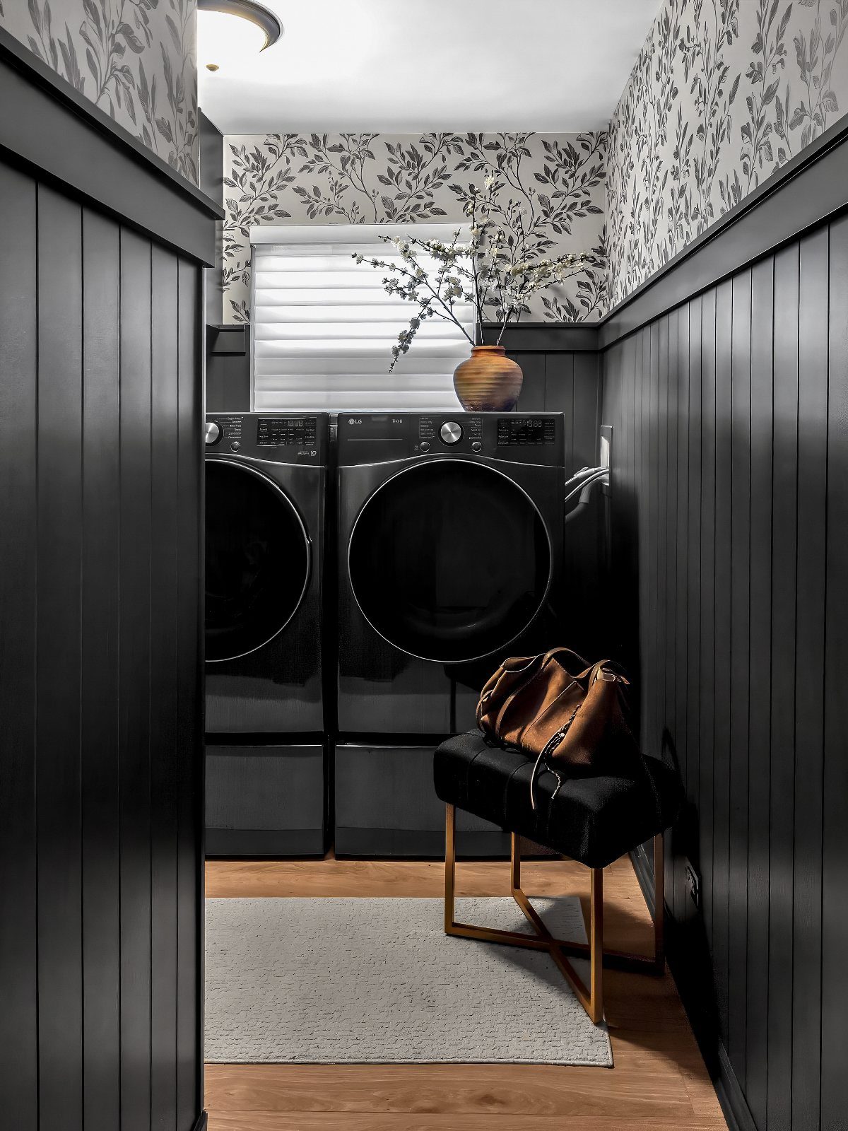 Laundry room with black beadboard walls and grey botanical patterned wallpaper above.