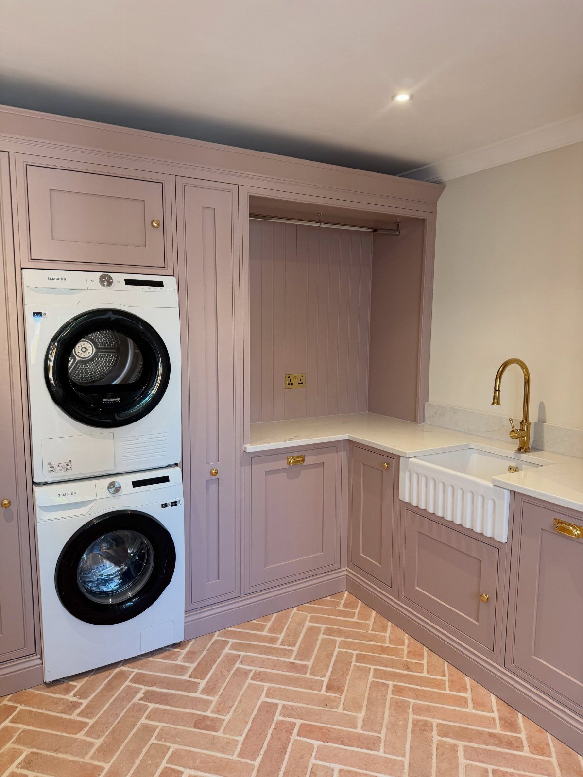 Laundry room with mauve cabinets, stacked washer dryer, and herringbone terracotta flooring.