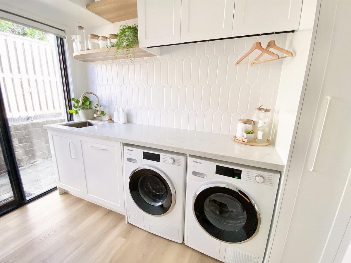 Bright laundry room with white cabinets and washing machines illuminated by natural light.