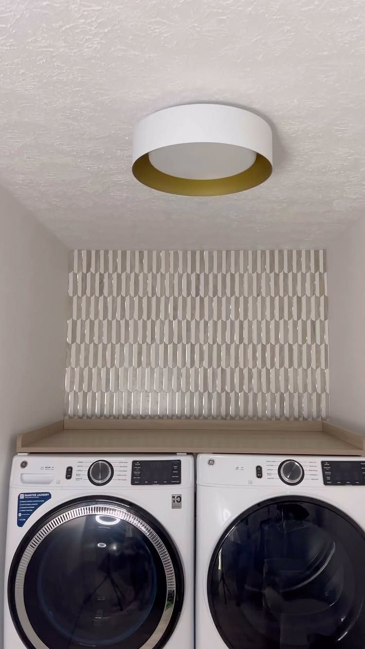 White cylindrical ceiling light illuminating a laundry room with white washer and dryer.