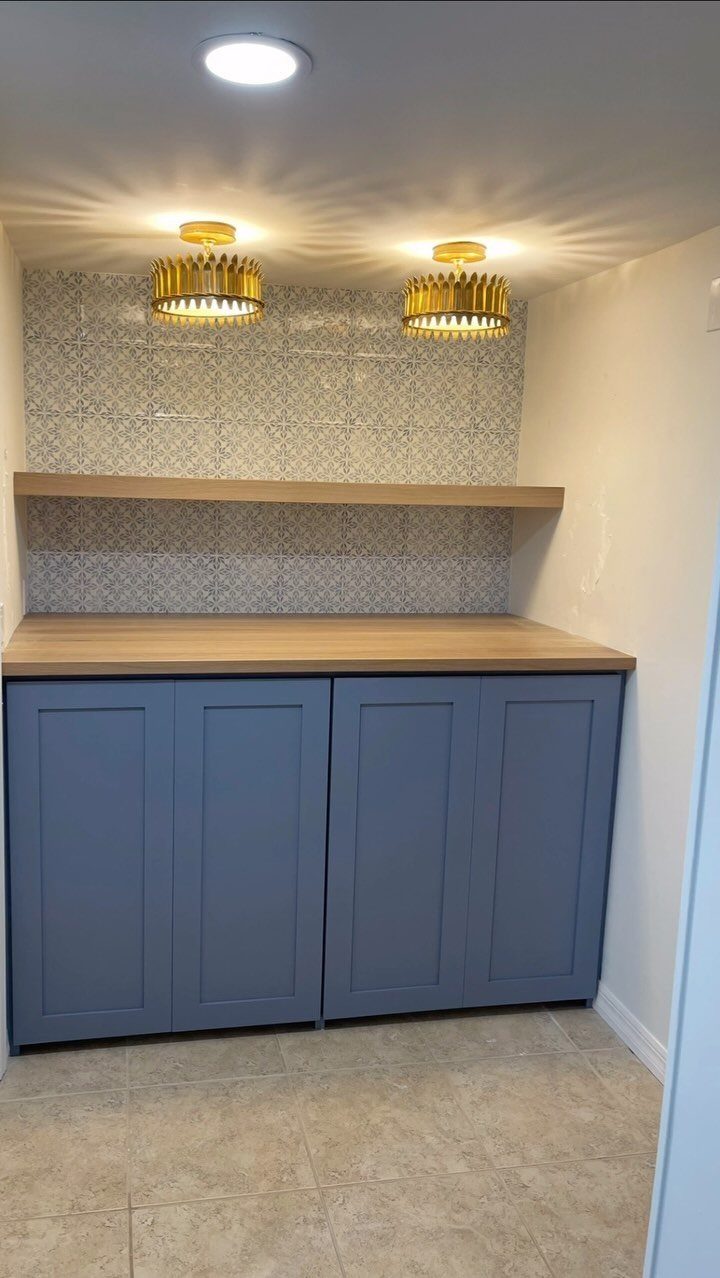 Blue cabinets and wood shelving illuminated by gold pendant and recessed ceiling lights.