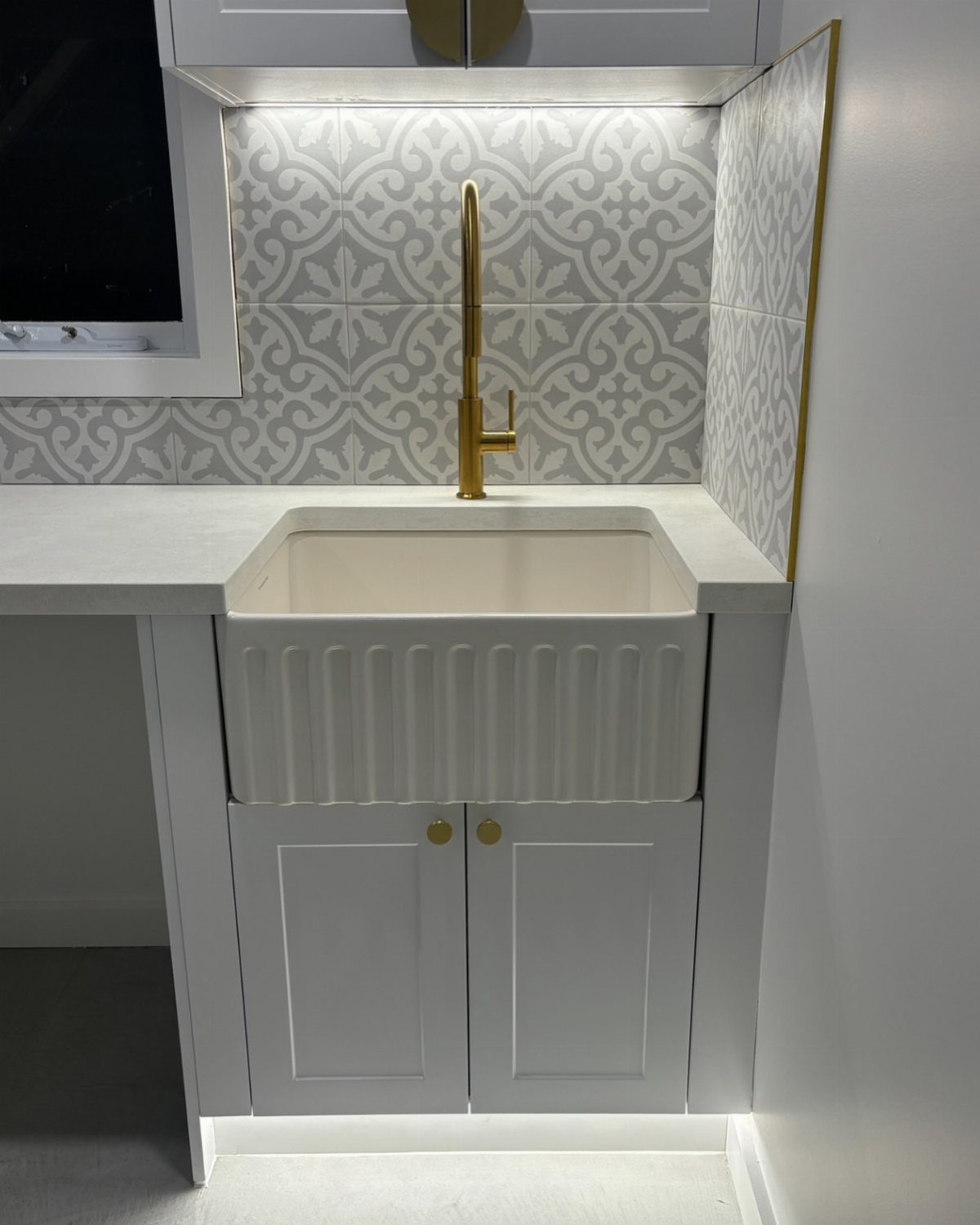 White laundry sink with gold faucet and LED under-cabinet and toe-kick lighting.