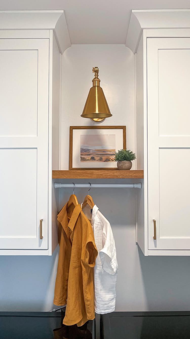 Gold wall sconce lighting a wooden shelf between white laundry room cabinets