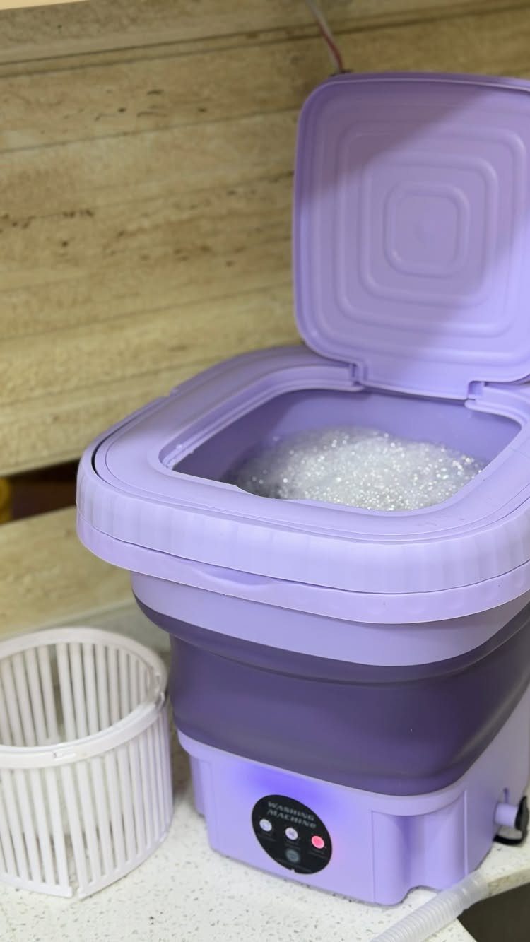 Purple portable washing machine with soapy water and a white laundry basket.