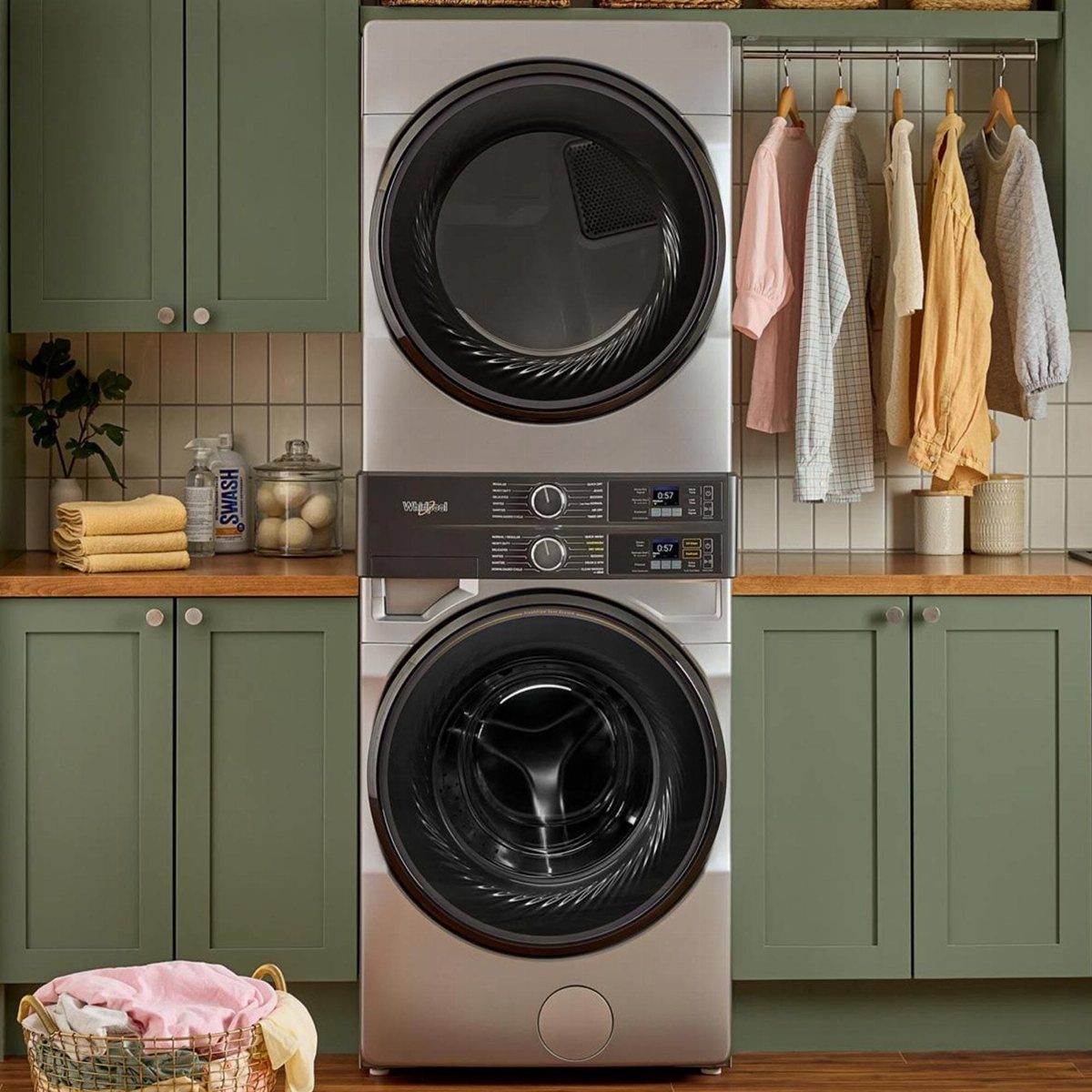 Silver stackable washer and dryer unit installed between green cabinets in a laundry room.